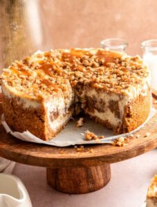 Apple crumble cheesecake sliced open on a wooden cake stand.