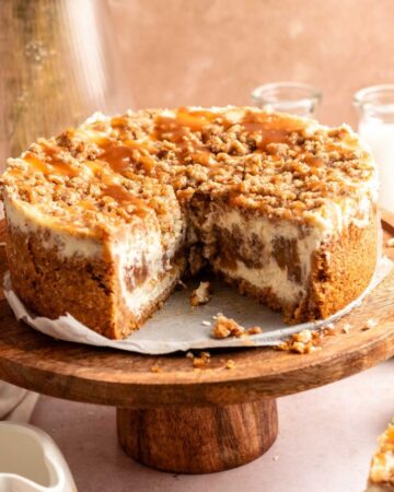 Apple crumble cheesecake sliced open on a wooden cake stand.