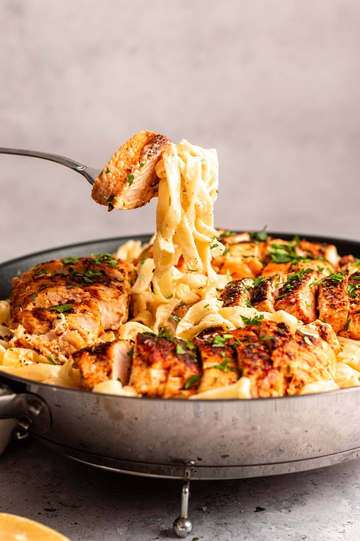 Fork lifting fettuccine with alfredo sauce from the pan with blackened chicken alfredo.