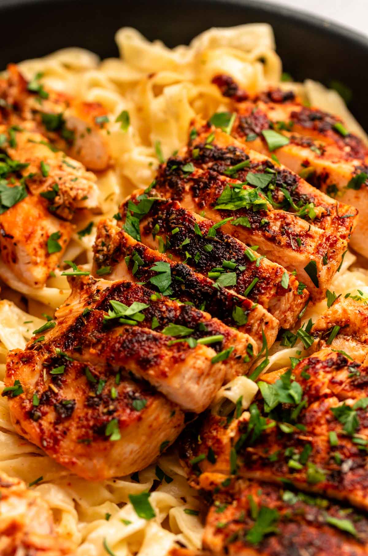 Sliced blackened chicken over a bed of fettuccine Alfredo.