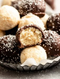 Pile of coconut balls on a plate with a bite missing from the middle one.