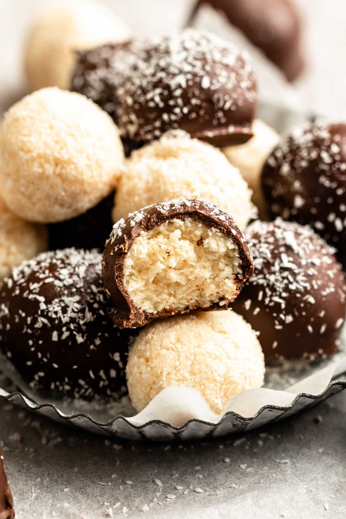 Pile of coconut balls on a plate with a bite missing from the middle one.