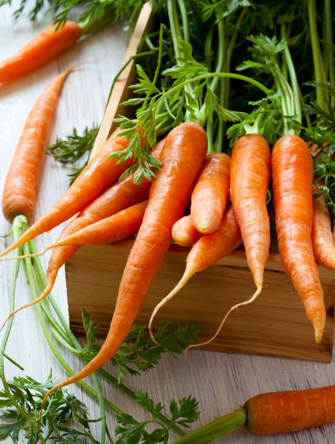 Whole carrots with their stems on a wooden box.