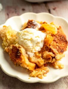 Plate with 4 ingredient peach cobbler with vanilla ice cream on top.