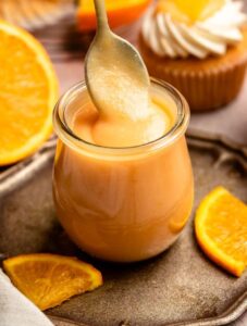 A jar with orange curd and a spoon.