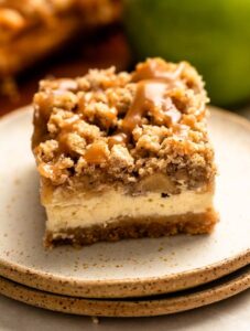Slice of caramel apple cheesecake bars on a stack of two plates.