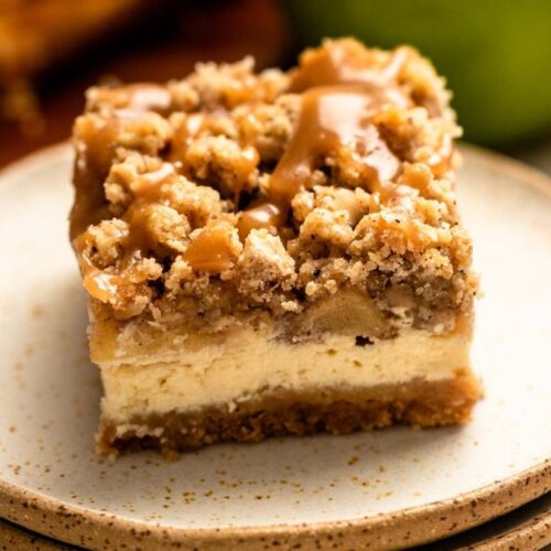 Slice of caramel apple cheesecake bars on a stack of two plates.