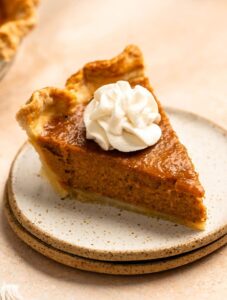 Close up shot of a slice of pumpkin pie with sweetened condensed milk and whipped cream on top.