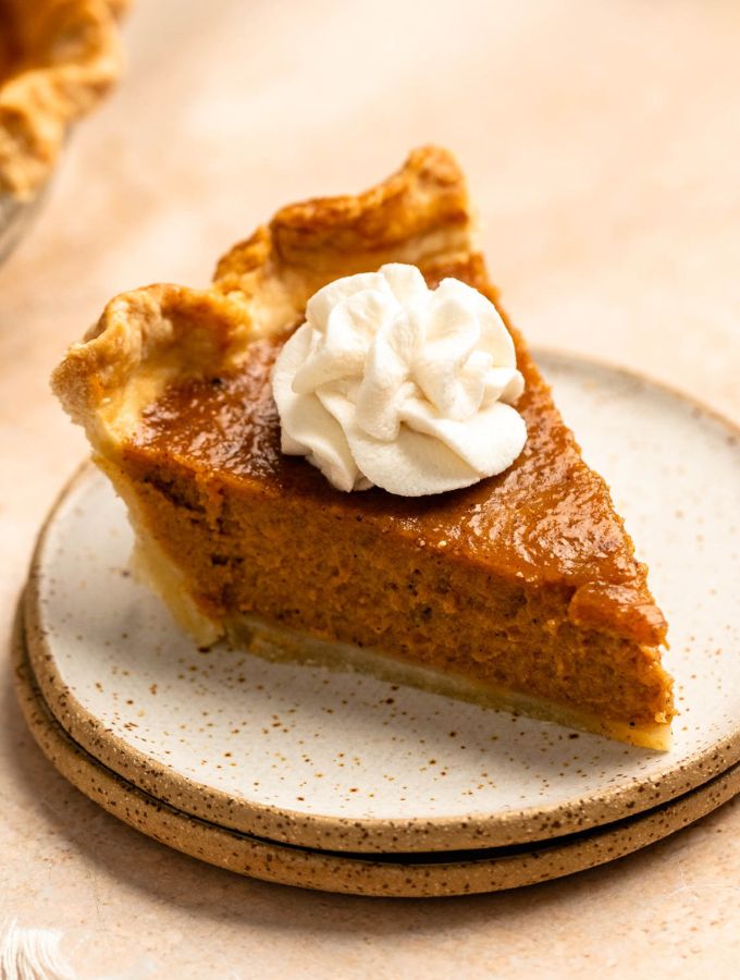 Close up shot of a slice of pumpkin pie with sweetened condensed milk and whipped cream on top.