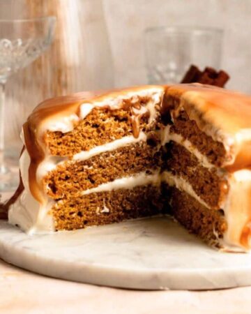 Slice missing from a pumpkin layer cake with cream cheese frosting and caramel sauce on top.