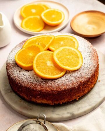 Orange olive oil cake on a marble cake plate.