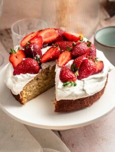 Slice missing from a strawberry whipped cream cake.