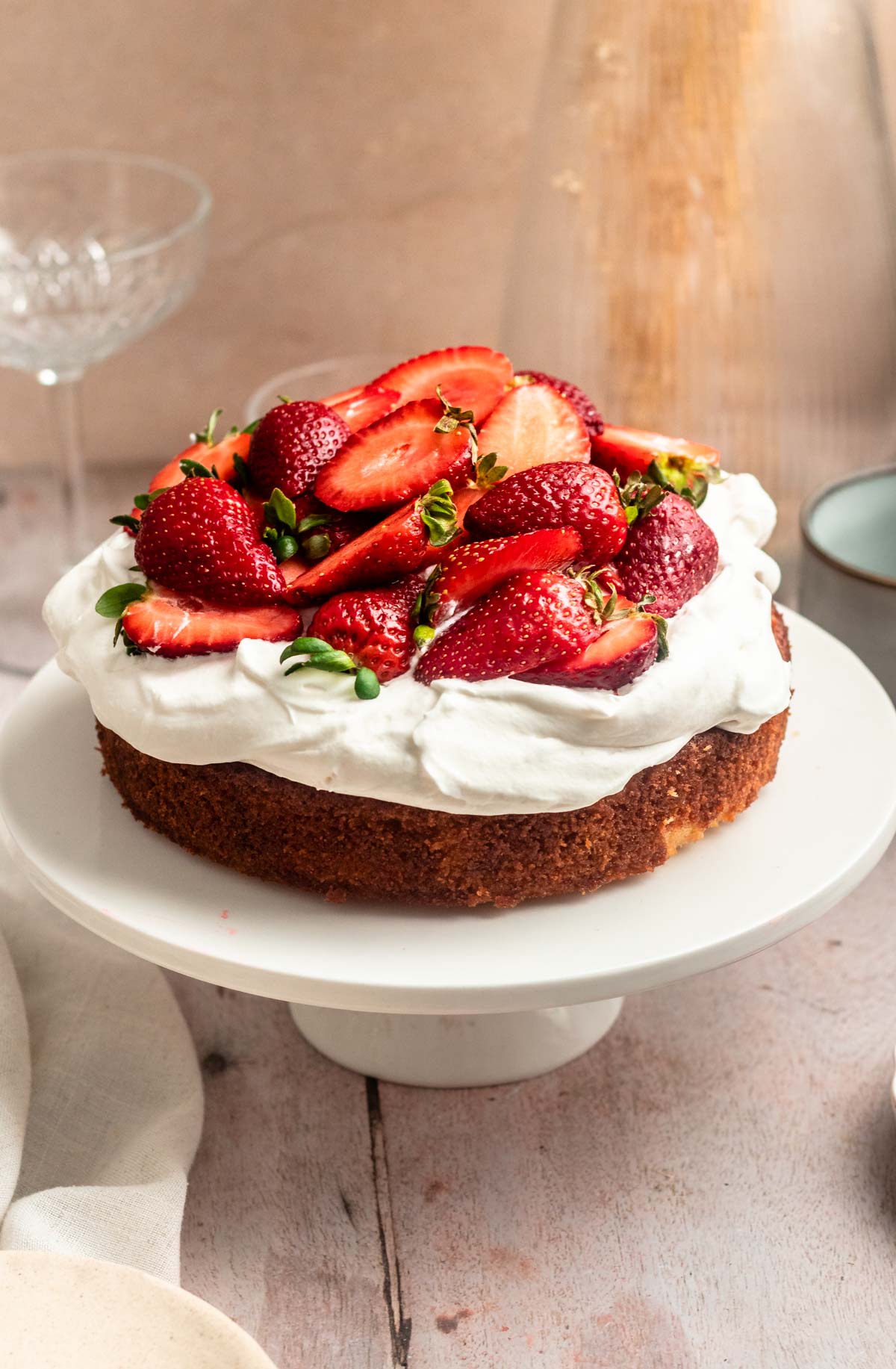 Strawberry whipped cream cake on a white cake stand.