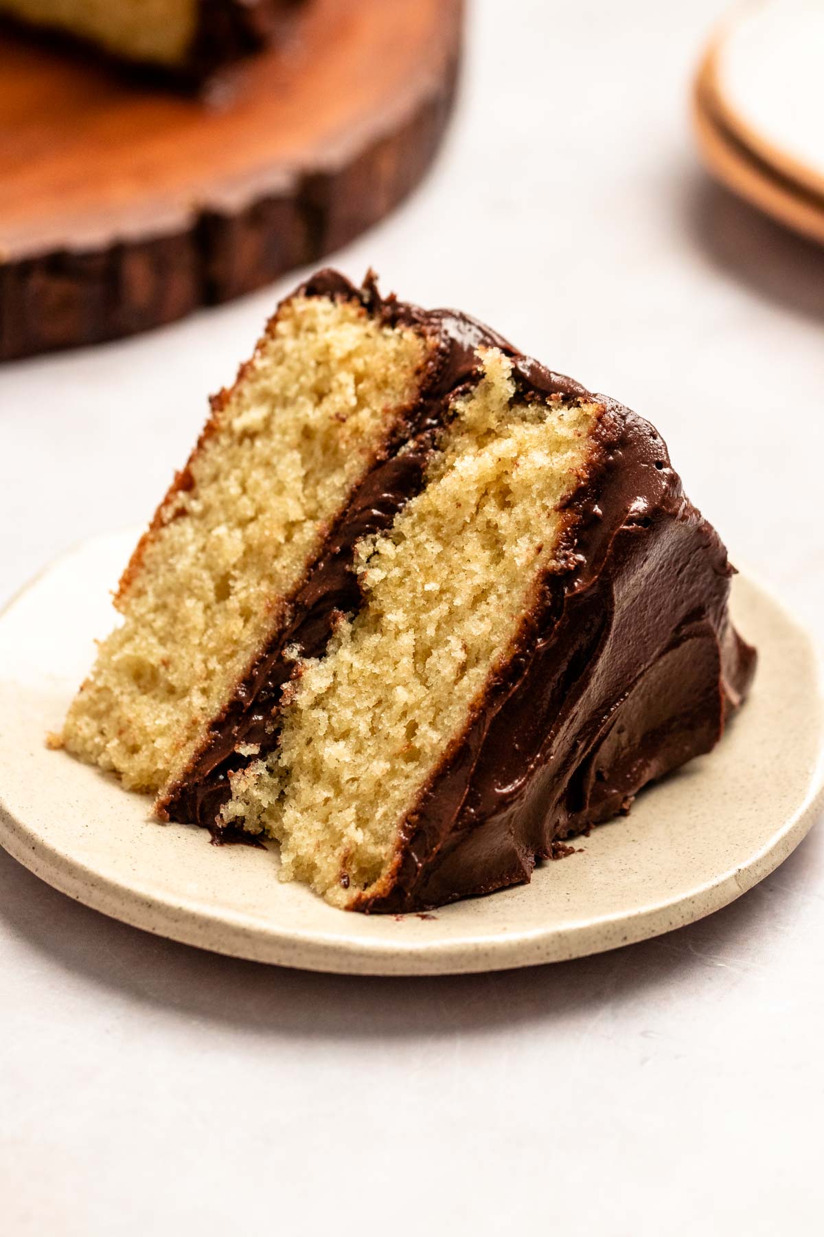 Slice of vanilla cake with chocolate frosting on a white plate.