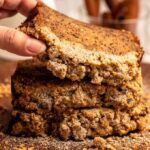 Hand lifting a slice of streusel banana bread from a stack of slices of banana bread.