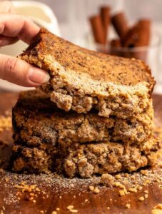 Hand lifting a slice of streusel banana bread from a stack of slices of banana bread.
