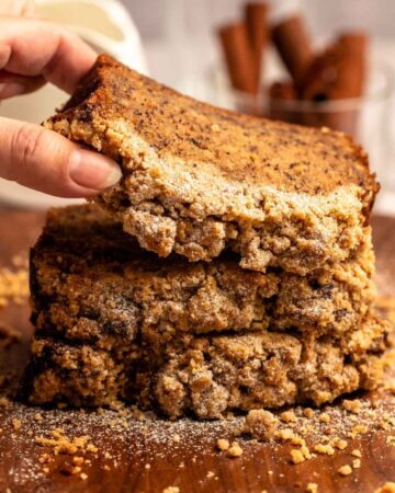 Hand lifting a slice of streusel banana bread from a stack of slices of banana bread.