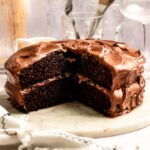 Slice missing from a chocolate cake with chocolate cream cheese frosting.