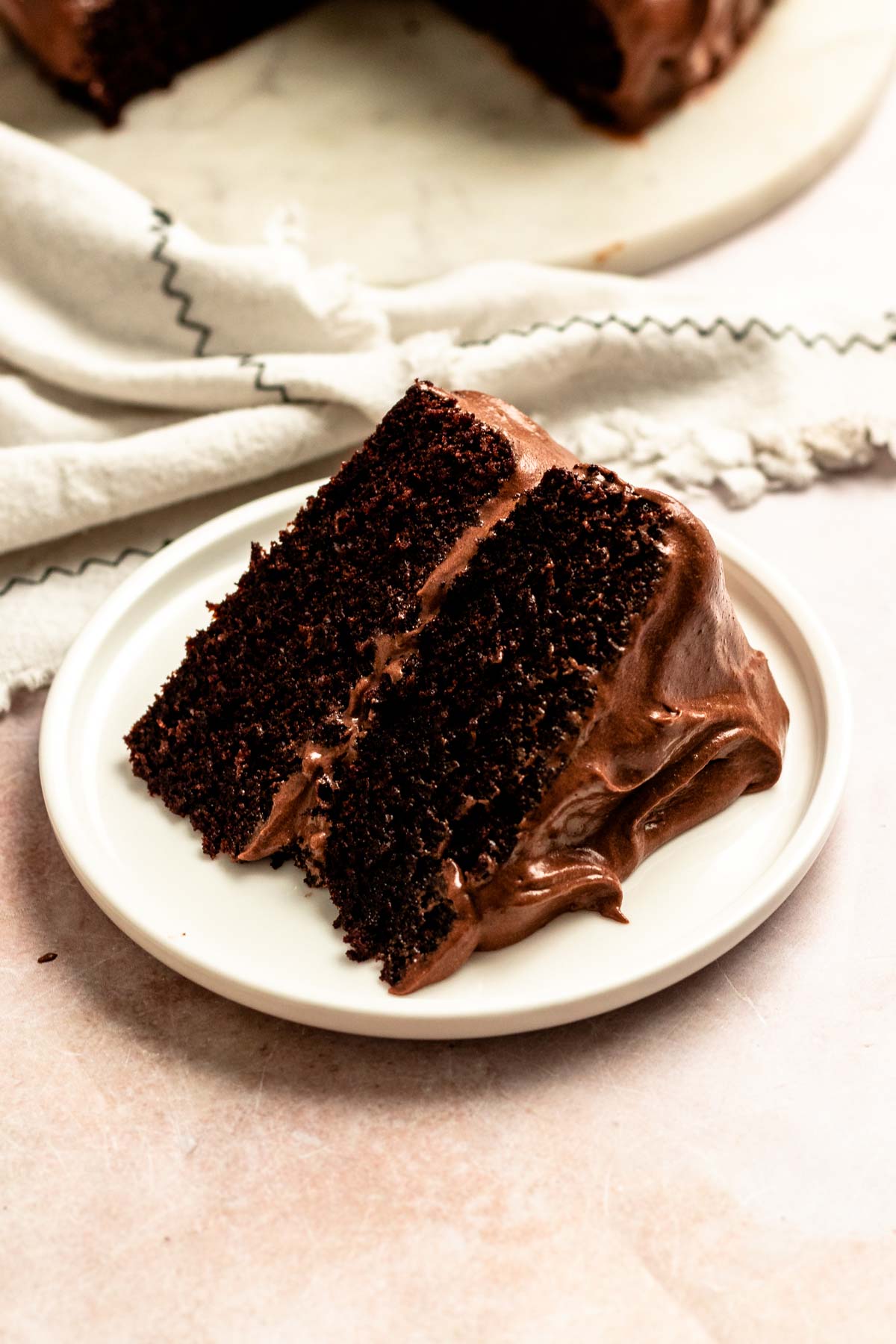 Slice of a chocolate cake with chocolate cream cheese frosting on a plate.