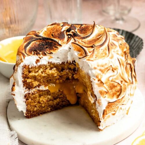 Slice missing from a lemon meringue cake on a cake plate.