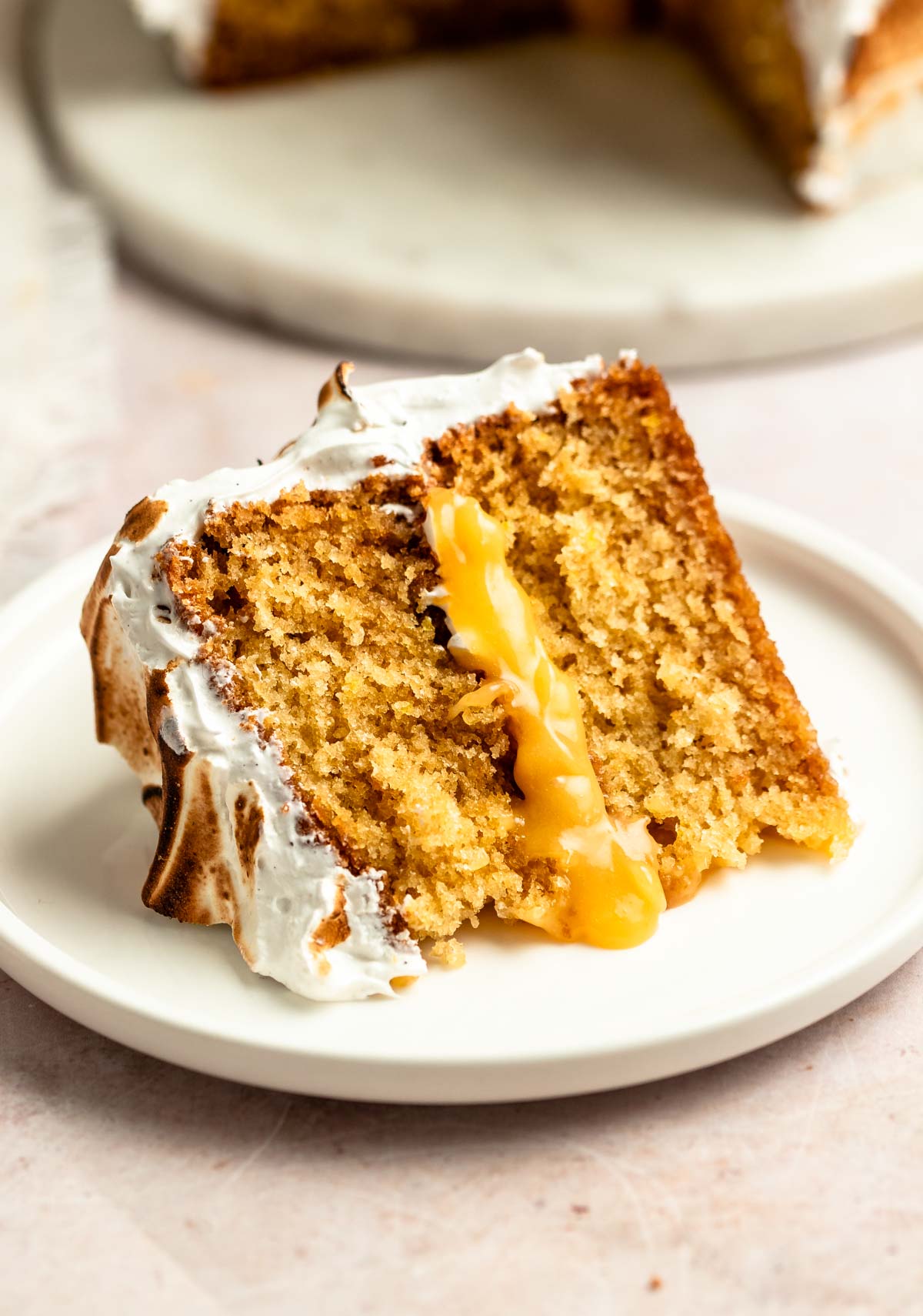 Slice of lemon meringue cake on a white plate.
