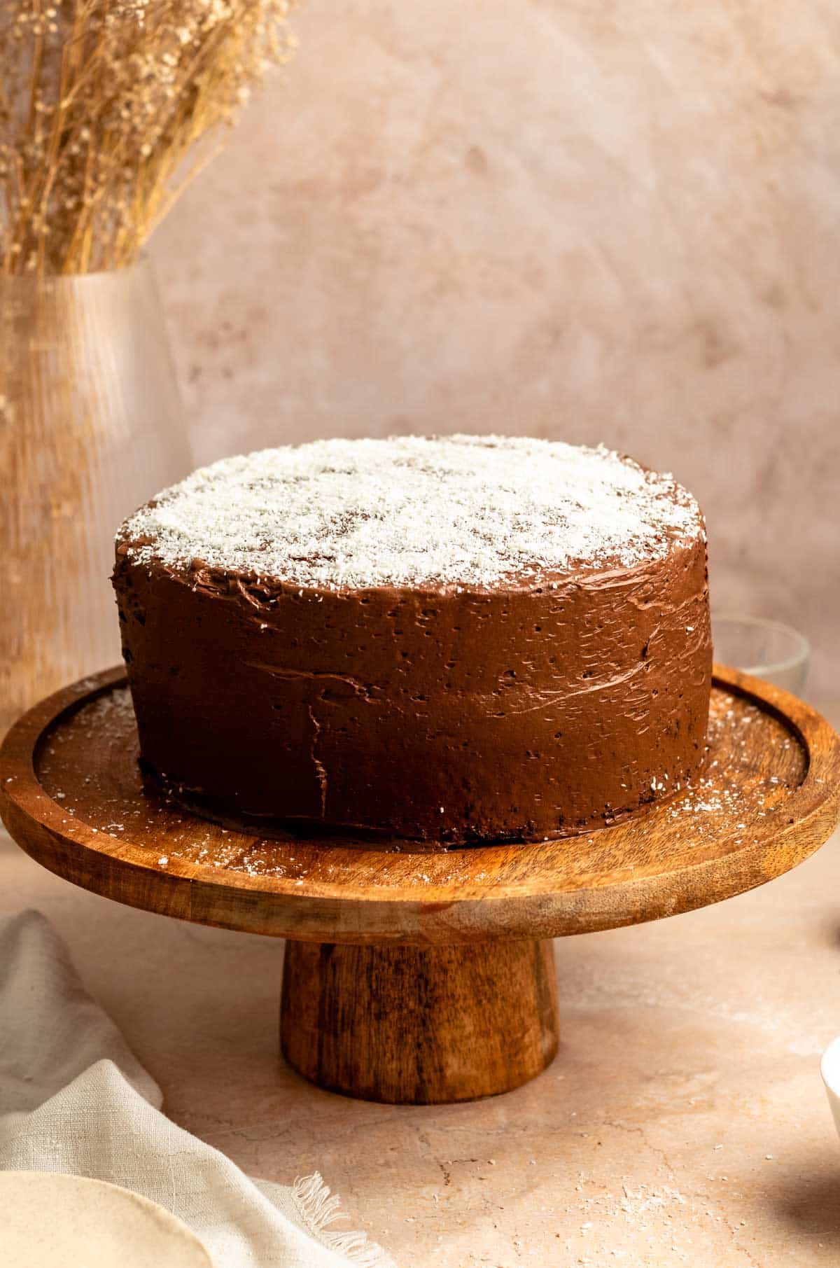 Chocolate coconut cake on a wooden cake stand.