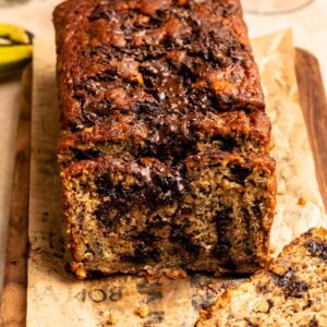 Sliced banana bread with chocolate chunks on a wooden board.