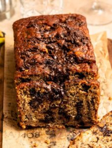 Sliced banana bread with chocolate chunks on a wooden board.
