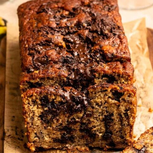 Sliced banana bread with chocolate chunks on a wooden board.
