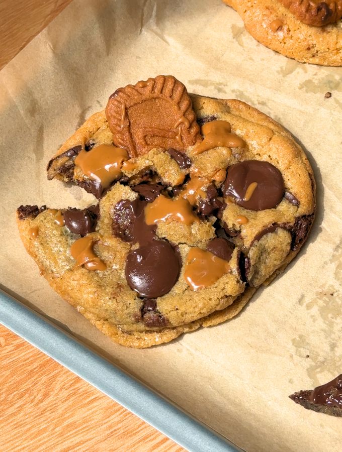 A close-up view of thick Biscoff butter cookies cut in half on a sheet of parchment paper, showing the soft, chewy interior texture and chocolate chips.