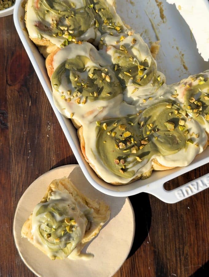 Pistachio cinnamon roll on a plate next to a baking pan.