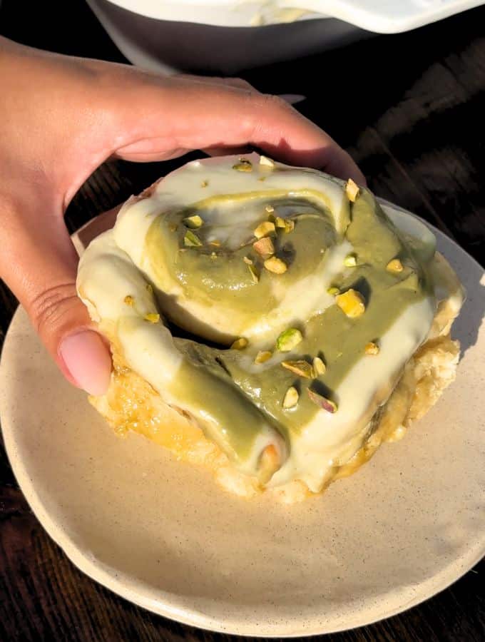 Plate with pistachio cinnamon roll on it with a hold grabbing it.