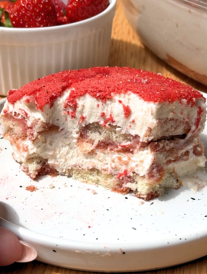 A single slice of strawberry tiramisu on a white plate showing distinct layers of soaked ladyfingers and pink mascarpone cream.