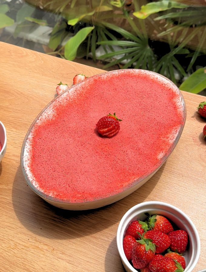 A wide, far-away shot of the full strawberry tiramisu in an oval baking dish, sitting on a beautifully decorated table with a summer theme.