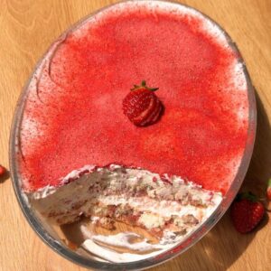 A top-down shot of a strawberry tiramisu in an oval baking dish with one slice cut out, showing the layered ladyfingers and pink cream inside the pan.