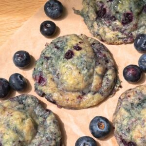 Blueberry cheesecake cookies on a brown parchment paper next to fresh blueberries.