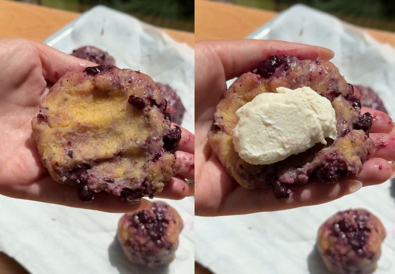A flattened piece of blueberry-swirled cookie dough held in a hand, with a rock-solid frozen cheesecake ball placed directly into the center.