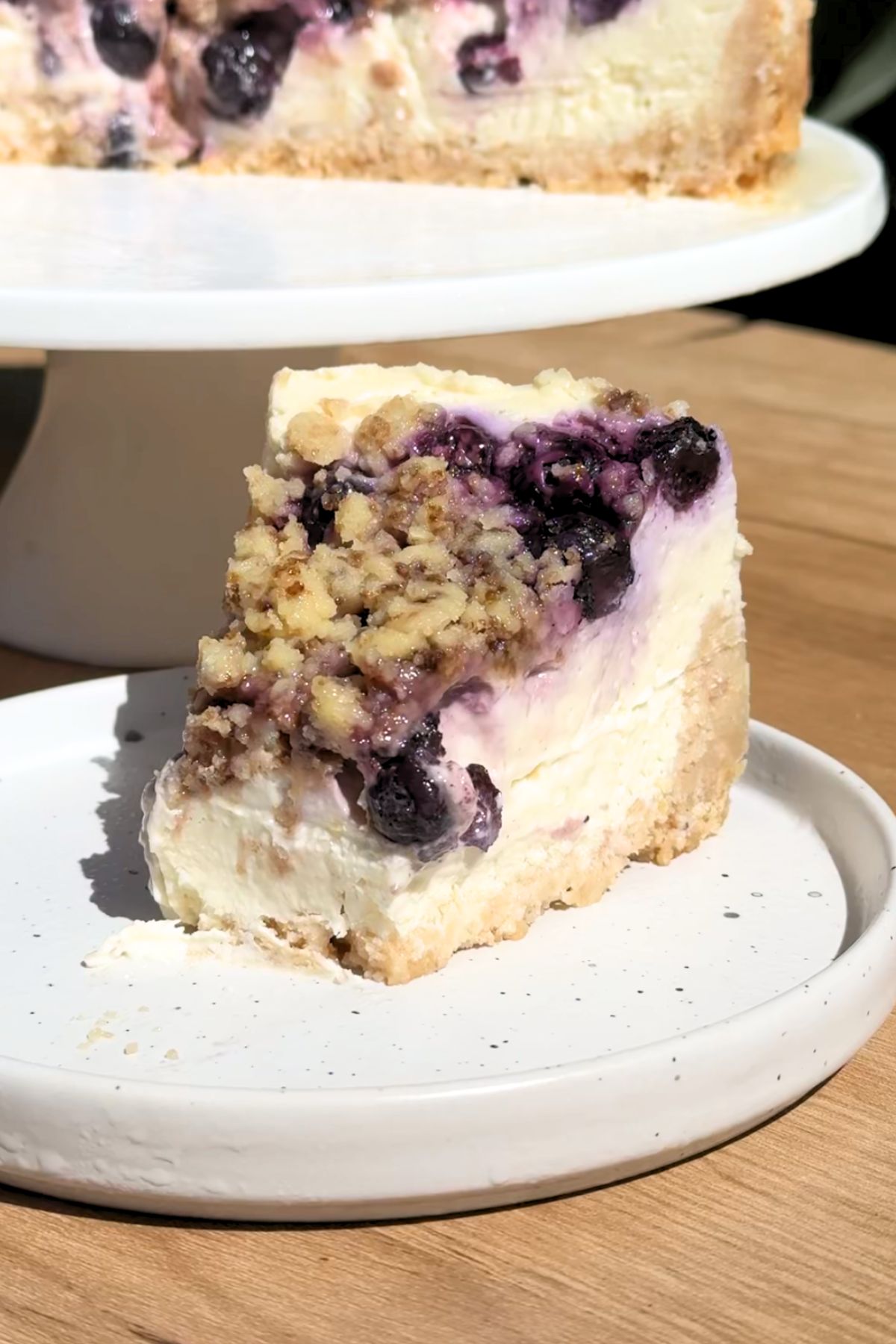 Bite missing from a slice of blueberry crumble cheesecake on a white plate.