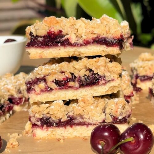 Stack of slices of cherry pie bars next to fresh cherries.