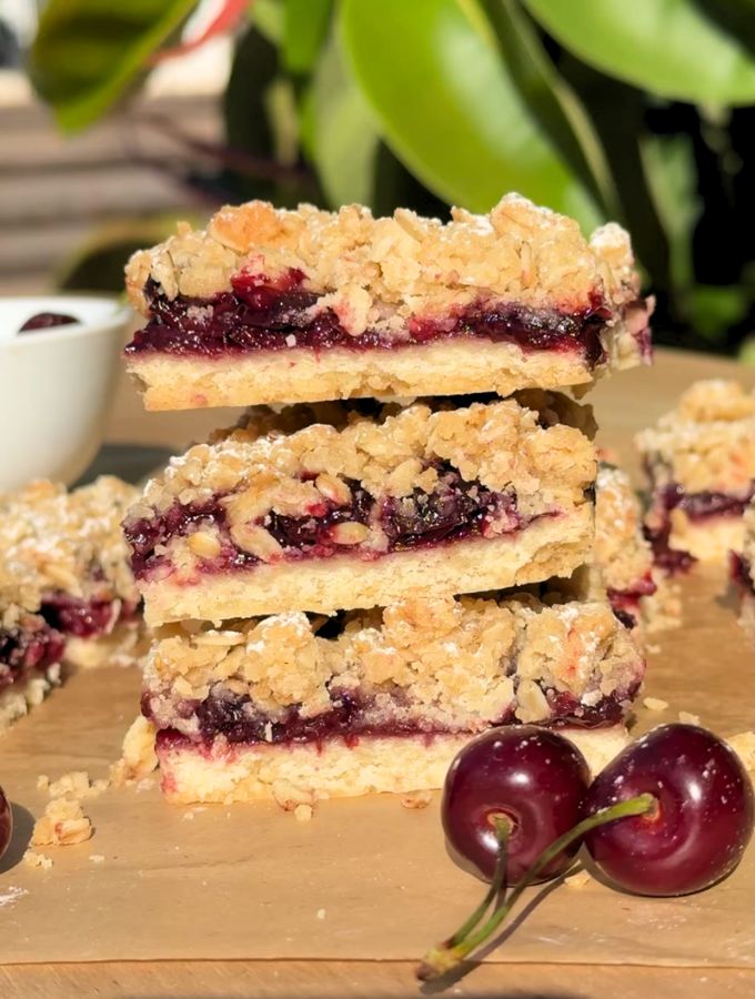 Stack of slices of cherry pie bars next to fresh cherries.