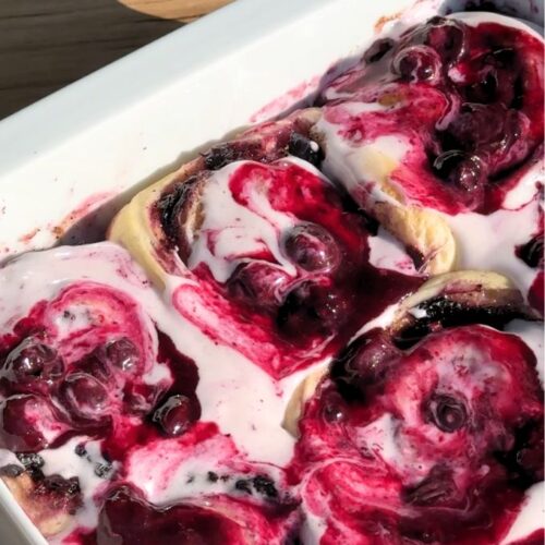 Blueberry cinnamon rolls with cream cheese frosting and blueberry sauce on top.