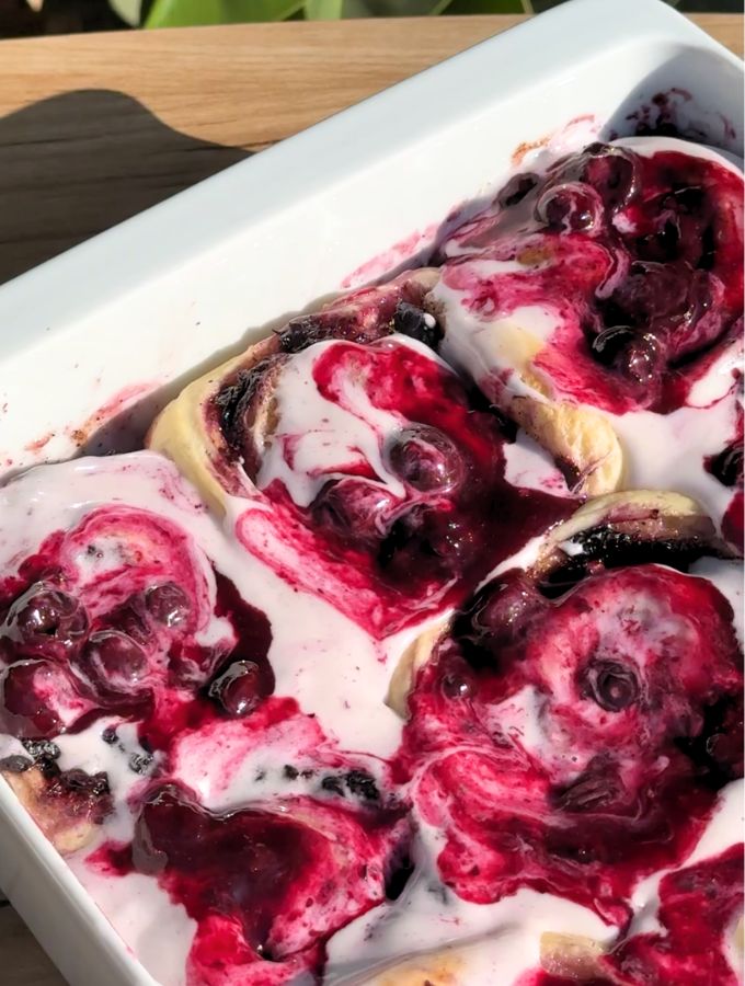 Blueberry cinnamon rolls with cream cheese frosting and blueberry sauce on top.