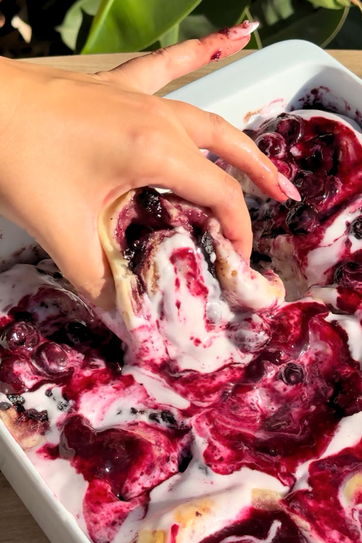 Hand lifting a blueberry cinnamon roll.