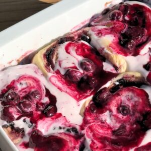 Blueberry cinnamon rolls with cream cheese frosting and blueberry sauce on top.