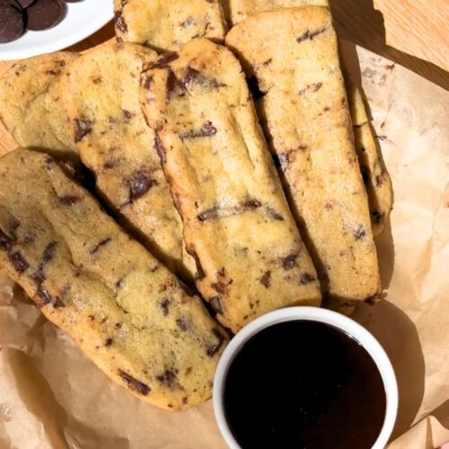 Chocolate chip cookie fries on a plate next to a bowl with chocolate sauce.
