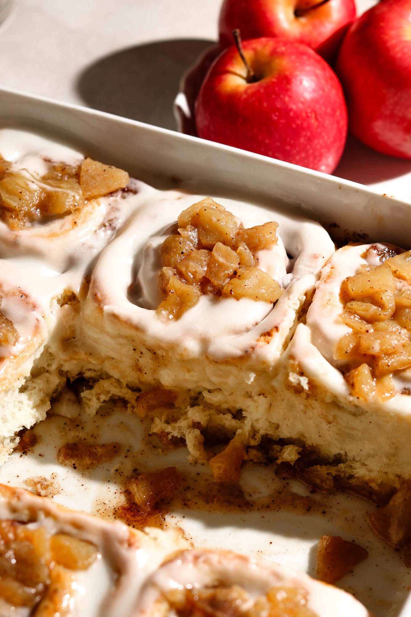 A pan of frosted apple cinnamon rolls with a portion removed, revealing the soft interior and gooey apple filling.