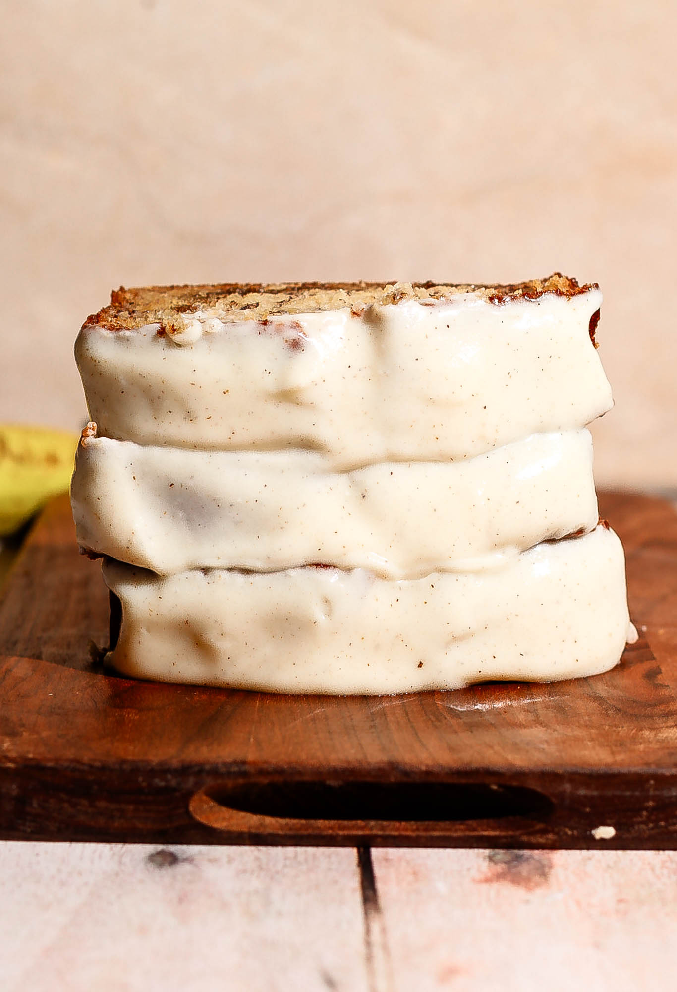 A vertical stack of frosted cinnamon roll banana bread slices resting on a wooden board.