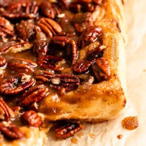 Extreme close-up of a warm pecan sticky bun generously topped with gooey caramel glaze and toasted pecan halves.