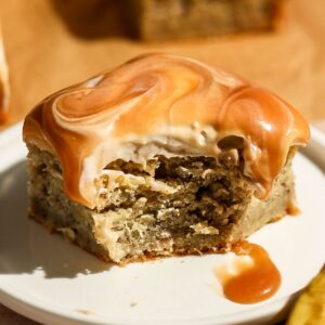 A final close-up view of a bitten slice of caramel banana cake on a white plate, showcasing the rich caramel glaze and soft crumb texture.