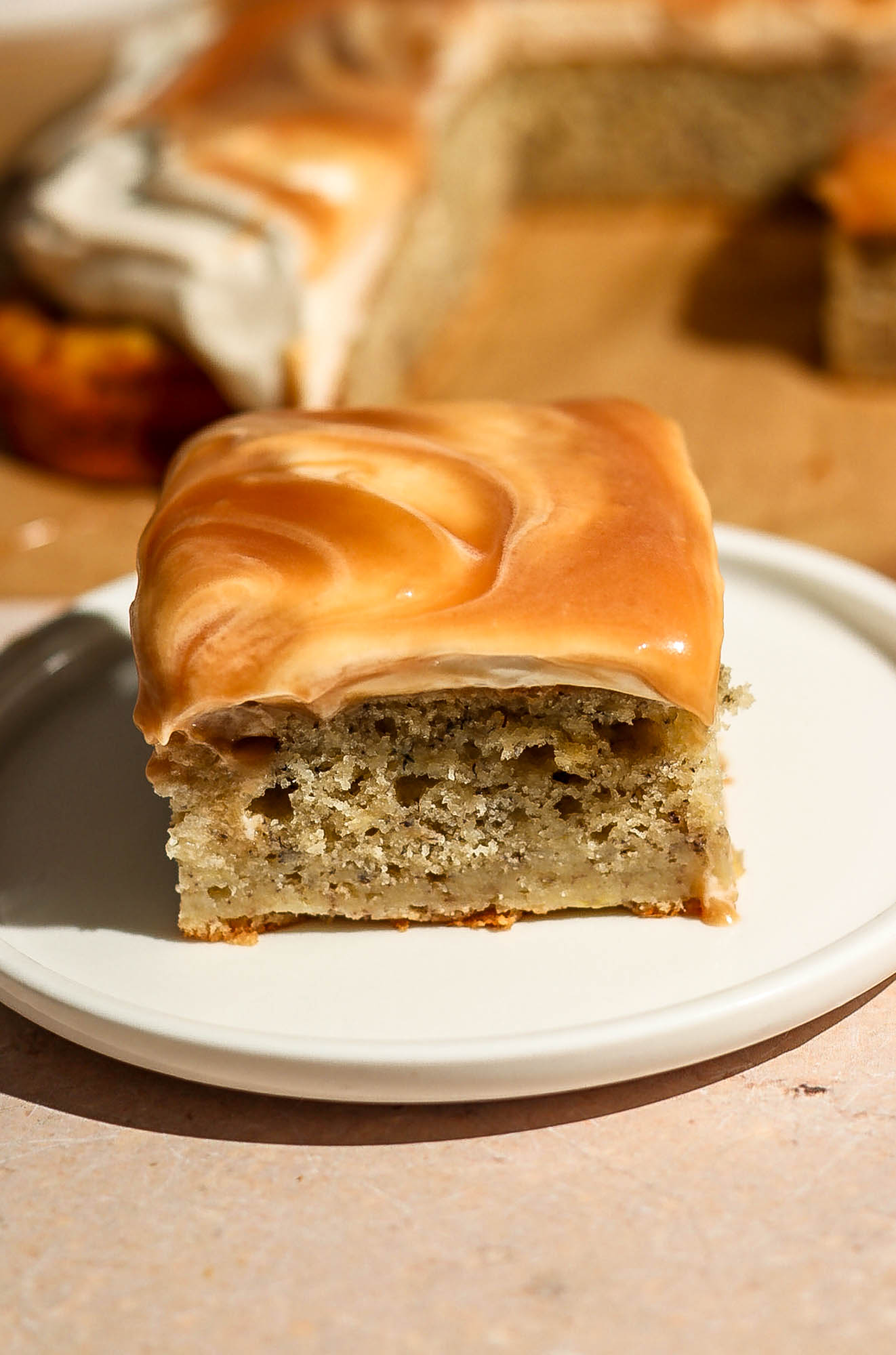 A single square slice of caramel banana cake on a white plate, showing its neat cut and the thick layer of swirled caramel frosting.